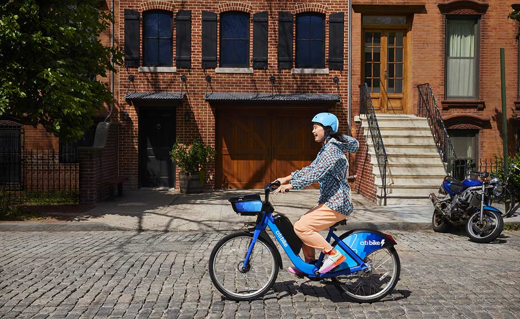 A woman rides a Citi Bike bicycle down a cobblestone street